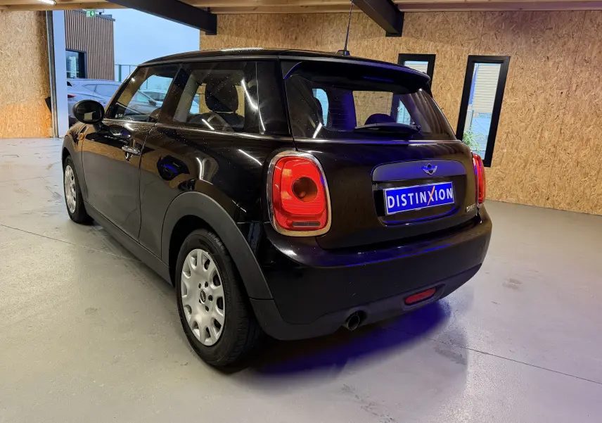 Vue 3/4 arrière droite d'une MINI One noire 2018 stationnée en intérieur avec feux arrière rouges et jantes argentées.