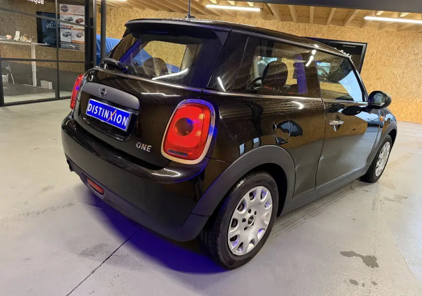 Vue 3/4 arrière droite d'une MINI One noire de 2018 avec feux arrière caractéristiques et jantes acier.