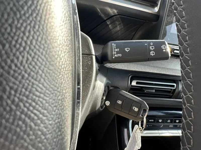 Gros plan sur la commande d'essuie-glace et la clé insérée côté gauche du volant dans l'habitacle gris d'une Citroën C3 2025.