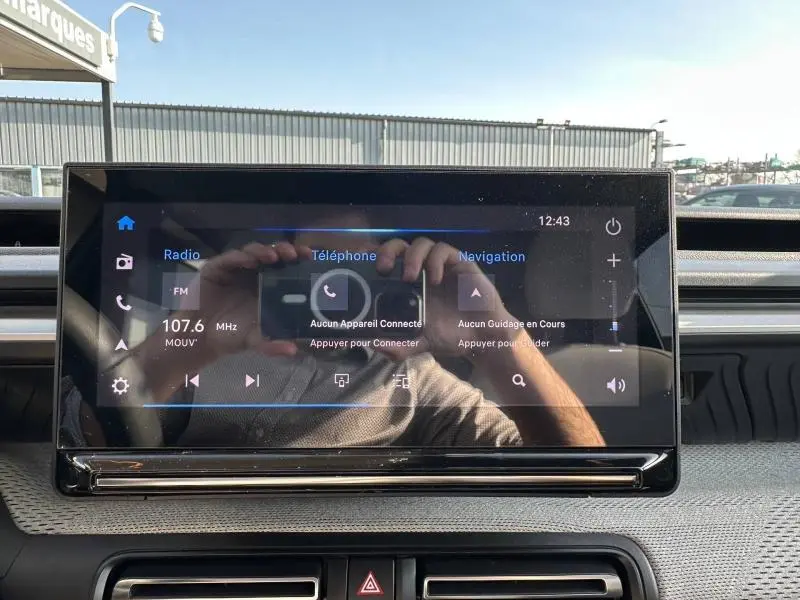 Écran tactile central de la Citroën C3 2025 affichant radio, téléphone et navigation, avec reflet du photographe visible.