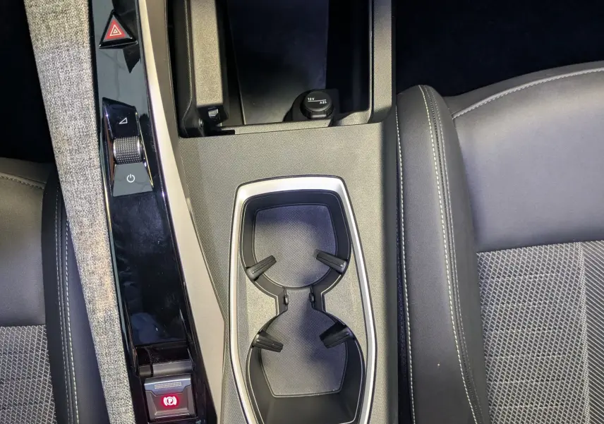 Vue plongeante sur la console centrale du Peugeot 5008 Hybrid 145 GT 2025, avec porte-gobelets et tissu gris clair.