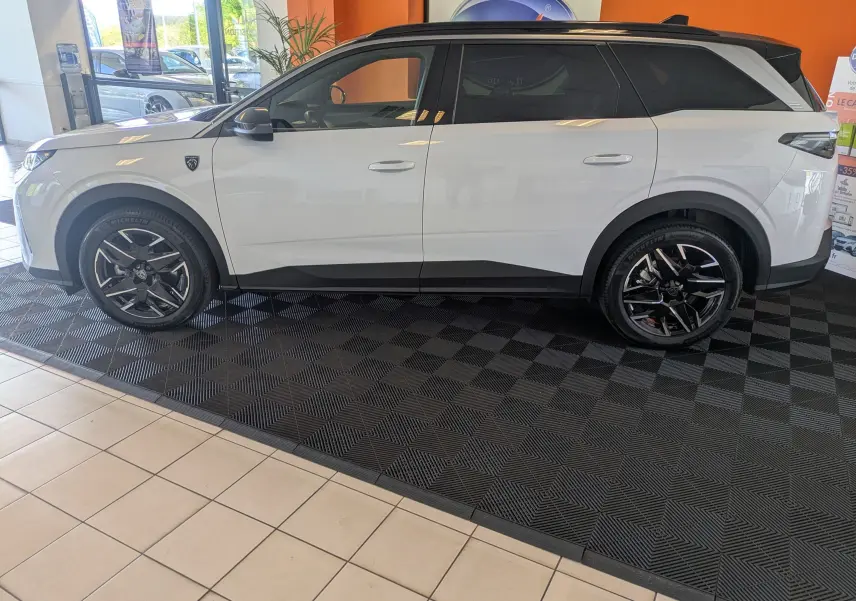 Peugeot 5008 Hybrid 145 e-DCS6 GT blanc Okenite avec toit noir, vue de profil côté gauche en intérieur showroom.