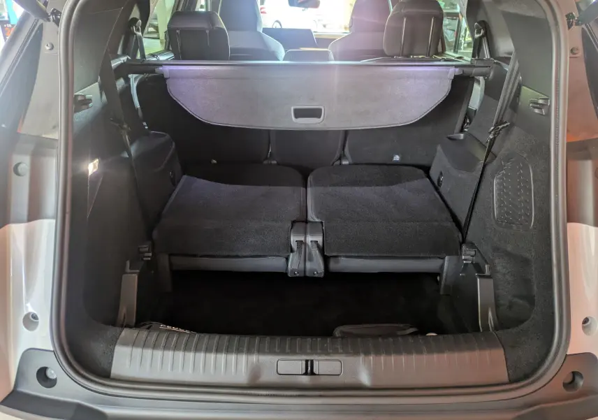 Coffre ouvert de la Peugeot 5008 Hybrid blanc Okenite, montrant les sièges arrière rabattus et la plage arrière noire.