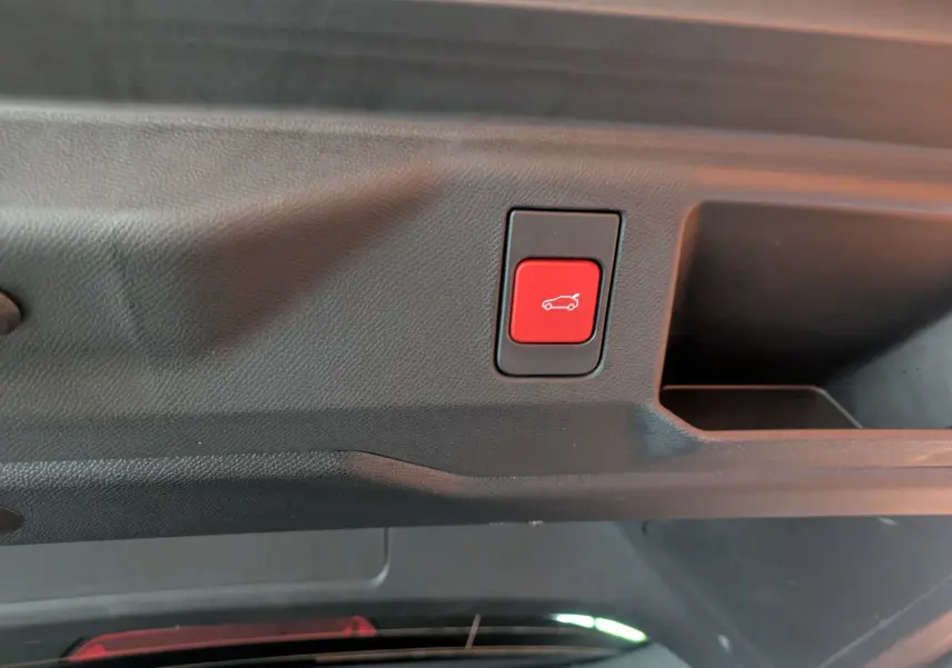 Bouton rouge d'ouverture électrique du hayon sur la garniture intérieure du coffre du Peugeot 5008 Hybrid blanc et toit noir.