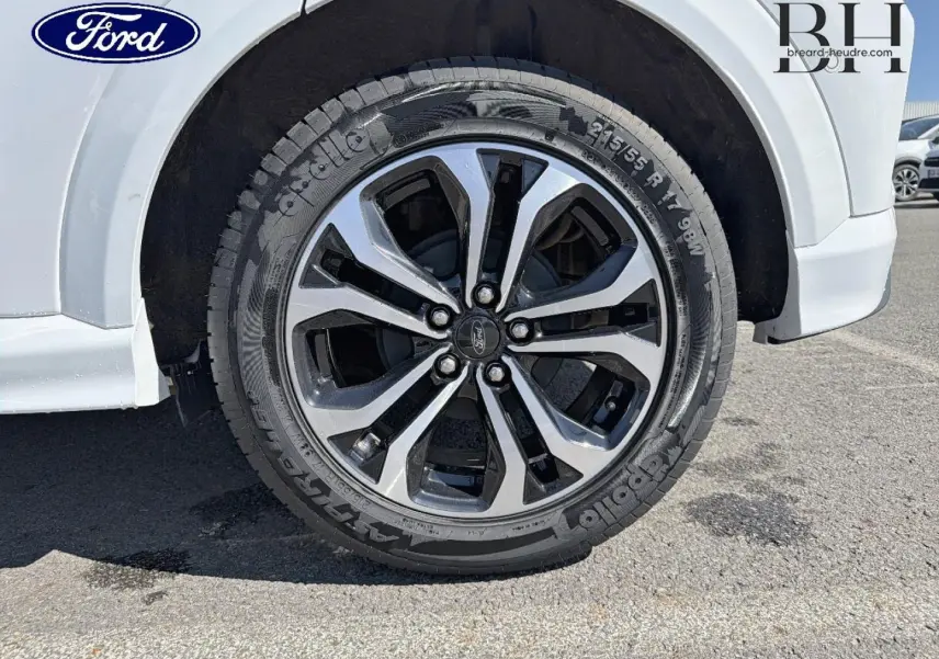 Gros plan sur la roue avant droite du Ford Puma blanc Glacier avec jante alliage bicolore et logo Ford central.