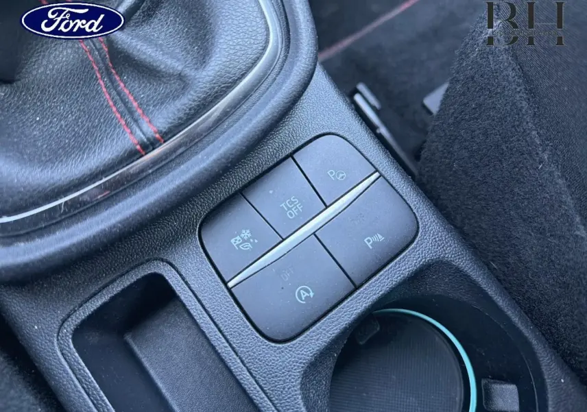 Gros plan sur la console centrale noire du Ford Puma 2023, avec boutons de contrôle et surpiqûres rouges visibles.
