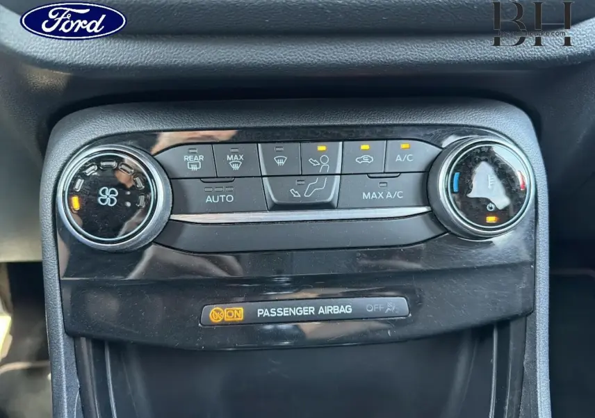 Vue rapprochée du tableau de bord noir du Ford Puma 2023 montrant les commandes de climatisation et l'indicateur airbag passager activé.