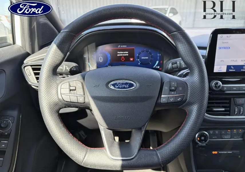 Vue rapprochée du volant sport en cuir noir avec surpiqûres rouges du Ford Puma 2023, tableau de bord digital et écran tactile visibles.