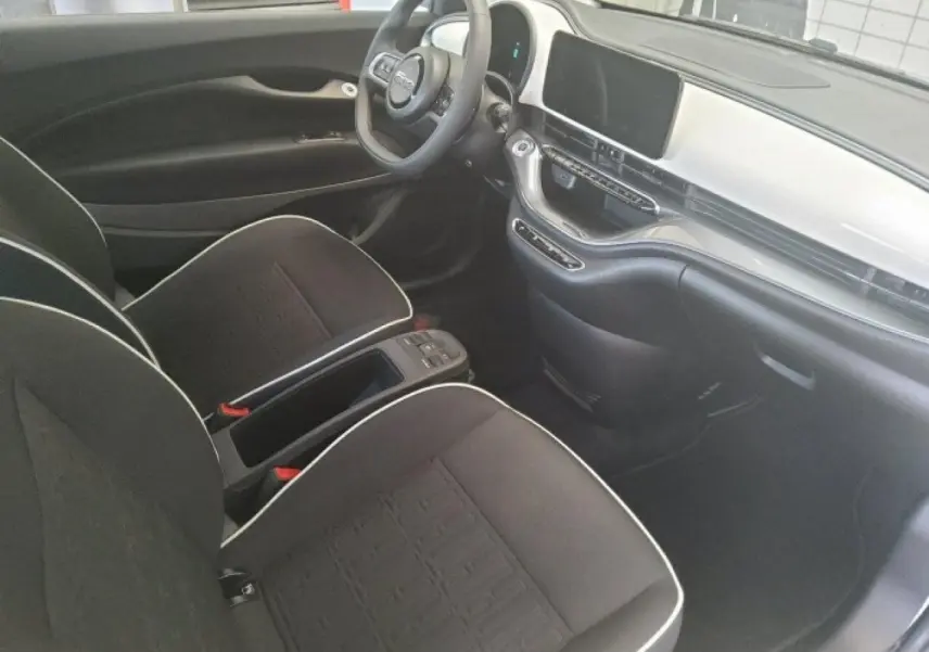 Vue intérieure côté conducteur de la Fiat 500 électrique 2024, sièges noirs avec surpiqûres blanches et tableau de bord blanc.