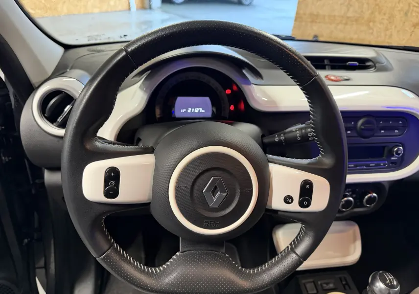 Vue rapprochée du volant cuir noir et blanc de la Renault Twingo III gris, avec tableau de bord et levier de vitesses manuel visibles.