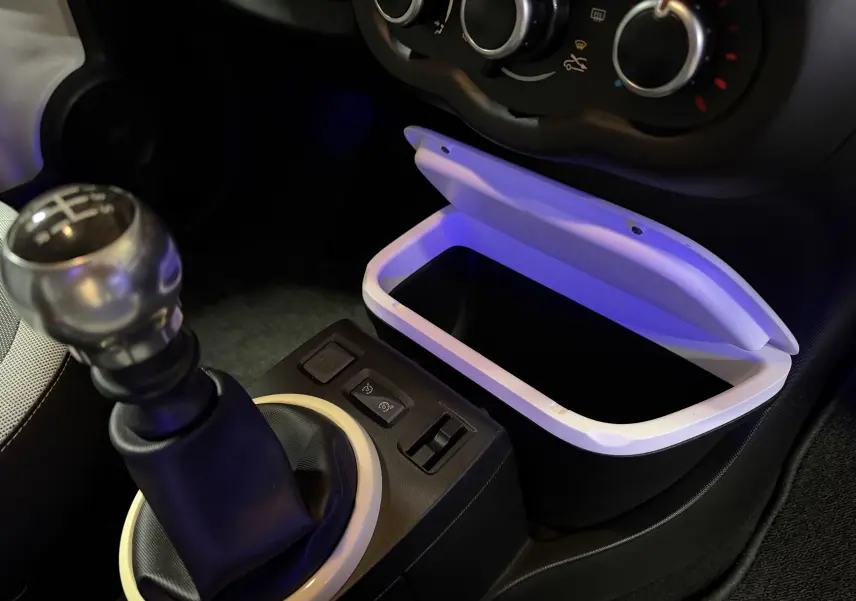 Gros plan intérieur sur la boîte manuelle et la console centrale ouverte avec éclairage bleu d’une Renault Twingo III gris.