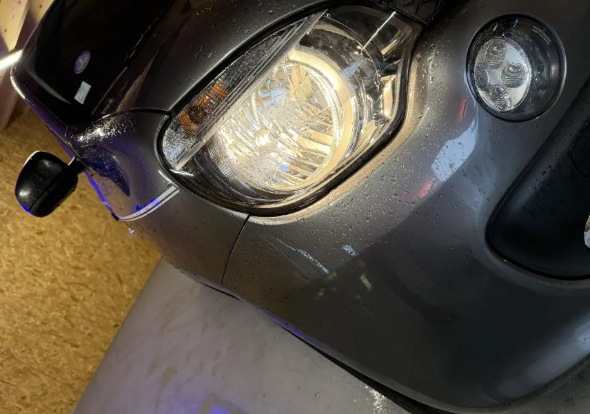 Gros plan sur l'avant droit gris d'une Renault Twingo III 2018, mettant en valeur le phare halogène et le rétroviseur noir.