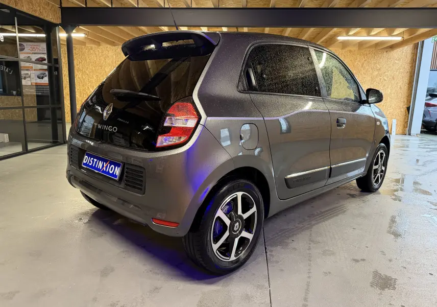 Renault Twingo III gris vue 3/4 arrière droit, avec jantes alliage et vitres teintées en intérieur d'atelier.