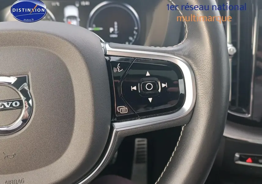 Gros plan sur le volant cuir noir multifonction du Volvo XC60 blanc, avec commandes intégrées et logo central visible.