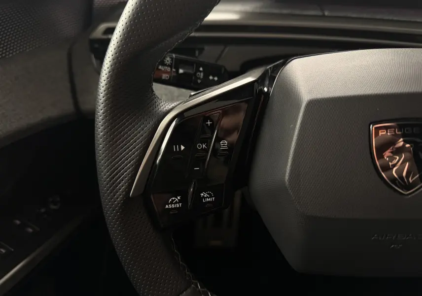 Gros plan sur le volant cuir perforé côté gauche du Peugeot 5008 Hybrid 145 e-DCS6 GT avec commandes intégrées.