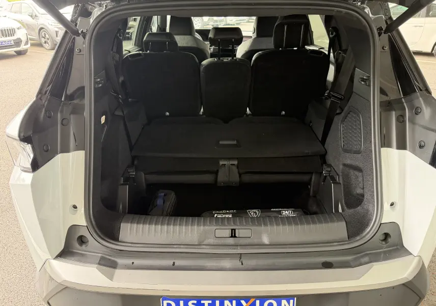Coffre ouvert en vue arrière d’un Peugeot 5008 Hybrid blanc Okenite avec intérieur noir et hayon électrique visible.