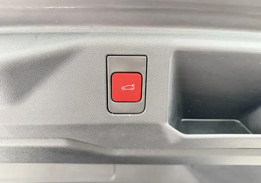 Bouton rouge d'ouverture électrique du hayon sur le panneau intérieur du coffre du Peugeot 5008 Hybrid 2025 blanc toit noir.