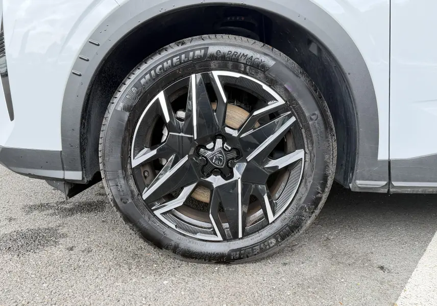 Gros plan sur la roue avant droite du Peugeot 5008 Hybrid blanc Okenite avec jante alliage noire et argentée.