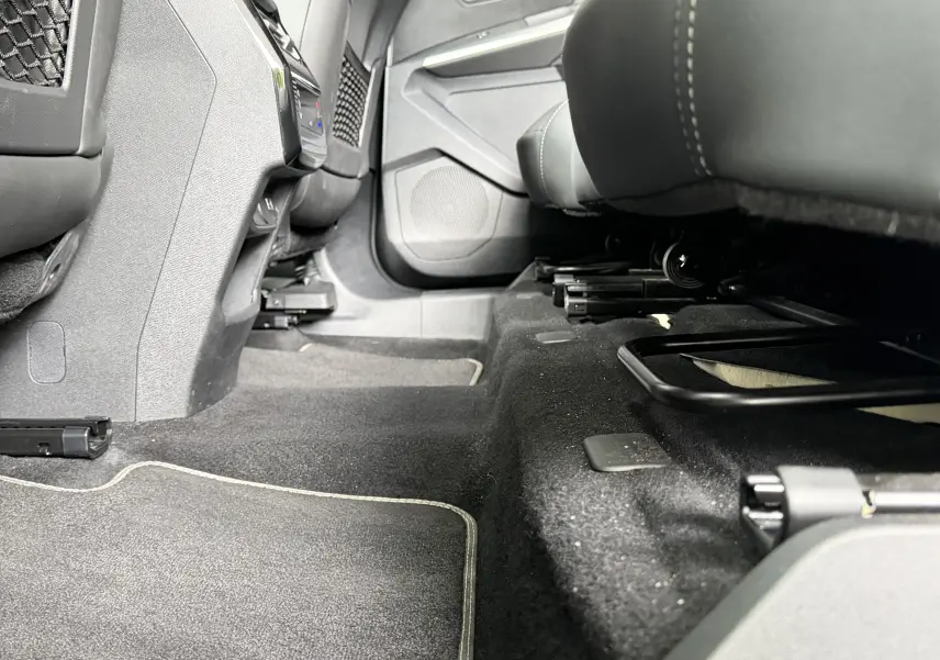 Vue intérieure sous les sièges avant du Peugeot 5008 Hybrid 145 e-DCS6 GT, tapis noir avec surpiqûres claires visibles.
