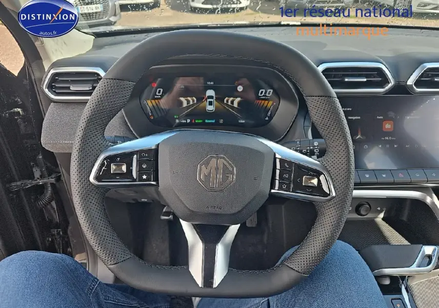 Vue intérieure centrée sur le volant noir perforé du MG ZS Hybrid 2026 avec tableau de bord numérique et écran tactile.
