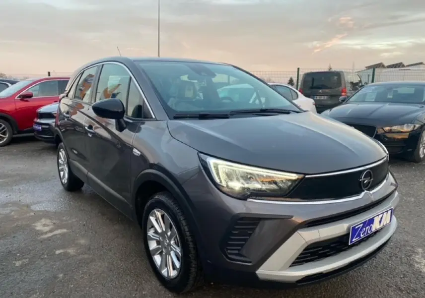 Opel Crossland gris magnetic en 3/4 avant droit, avec jantes alliage 16'' et phares allumés, stationné en extérieur.