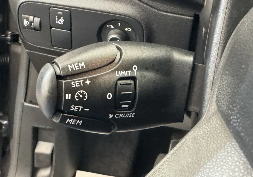 Gros plan sur la commande de régulateur de vitesse du côté gauche du volant cuir d'une Citroën C3 gris foncé 2020.