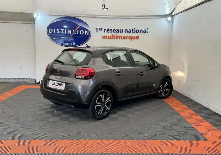 Citroën C3 gris foncé vue 3/4 arrière droit, avec protections latérales noires et jantes bicolores.