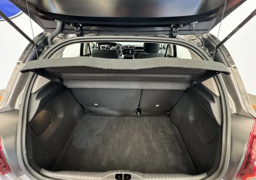 Coffre ouvert vu de l'arrière d'une Citroën C3 gris foncé, banquette arrière et tableau de bord visibles.