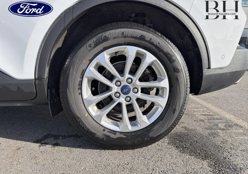 Gros plan sur la roue avant gauche avec jante alu du Ford Kuga blanc Glacier, montrant le pneu Yokohama et l'aile arrière.