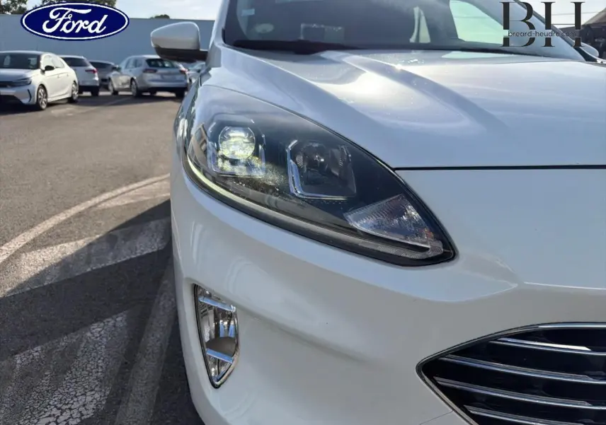Gros plan sur l'avant droit du Ford Kuga blanc Glacier, mettant en valeur le phare LED et la calandre chromée.