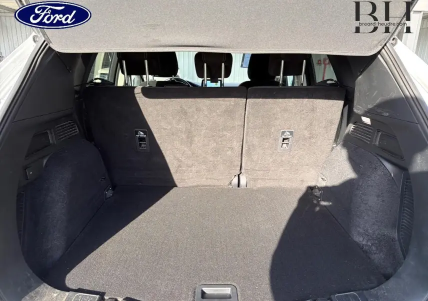 Coffre ouvert du Ford Kuga blanc Glacier 2021, montrant l'espace de chargement et la banquette arrière rabattable.