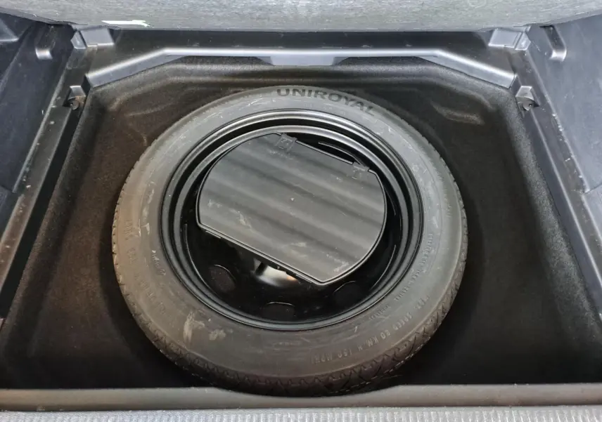 Roue de secours noire Uniroyal dans le coffre du Peugeot 3008 gris Artense, vue plongeante sur le pneu de secours.