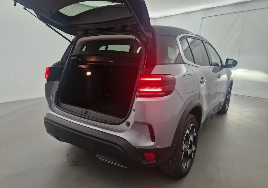 Vue 3/4 arrière droit du Citroën C5 Aircross gris Artense avec coffre ouvert et feux arrière allumés.