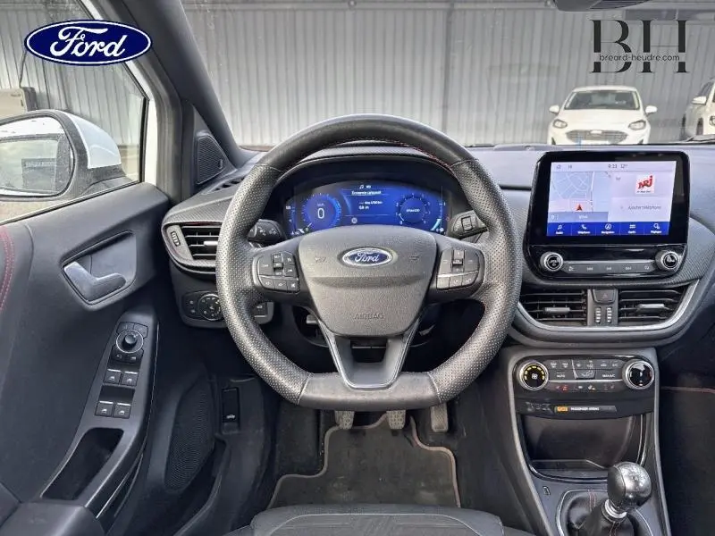 Vue intérieure frontale du tableau de bord et volant sport de la Ford Puma blanc glacier, avec écran tactile et commandes au volant.