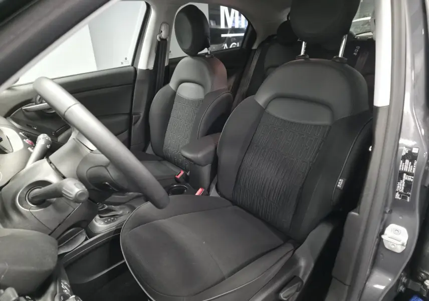 Intérieur de la Fiat 500X 2024 en gris, vue côté conducteur montrant sièges noirs avec monogramme FIAT et accoudoir central.
