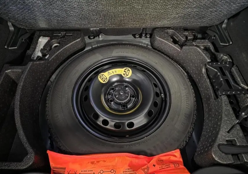 Gros plan sur la roue de secours noire dans le coffre d'une Fiat 500X 2024 gris, avec kit de sécurité orange visible.