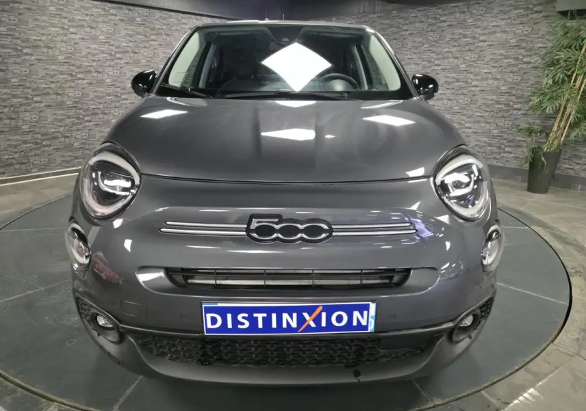 Vue frontale d'une Fiat 500X 2024 gris métallisé avec logo 500 distinctif et projecteurs LED ronds allumés.