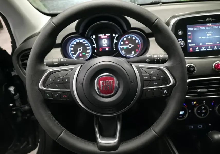 Vue rapprochée du volant noir de la Fiat 500X 2024 avec commandes intégrées et tableau de bord numérique éclairé.