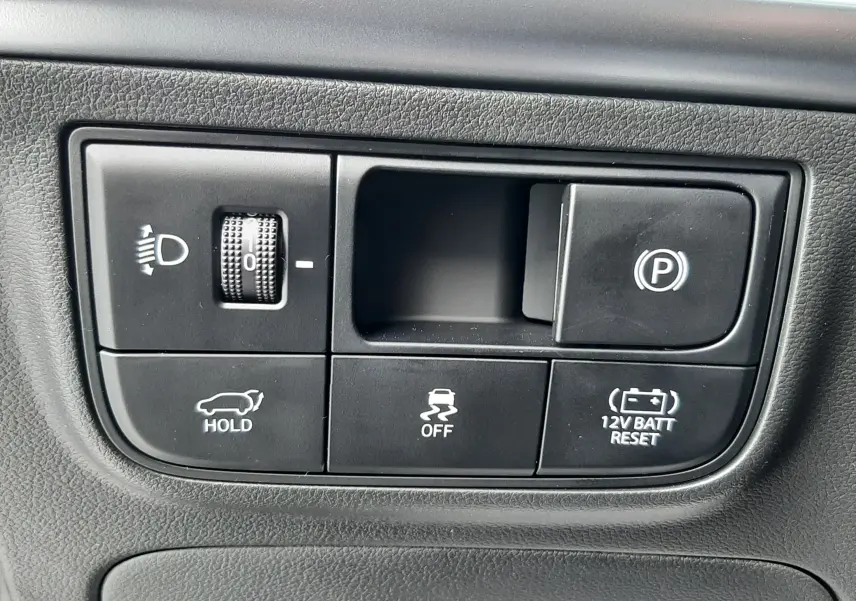 Panneau de commandes noir avec boutons de réglage des phares, frein à main électrique et fonctions d'assistance dans un Hyundai Tucson gris Ecotronic.