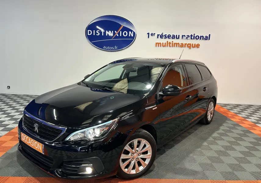 Peugeot 308 SW noire vue en 3/4 avant droit, avec jantes alliage et feux allumés dans un showroom.