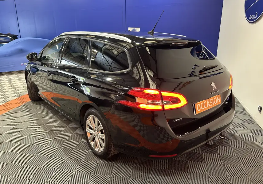 Peugeot 308 SW noire vue 3/4 arrière droit en intérieur, feux arrière allumés et attelage visible.