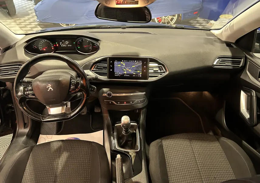 Vue intérieure avant de la Peugeot 308 SW noire, montrant le tableau de bord avec écran GPS et volant cuir multifonction.