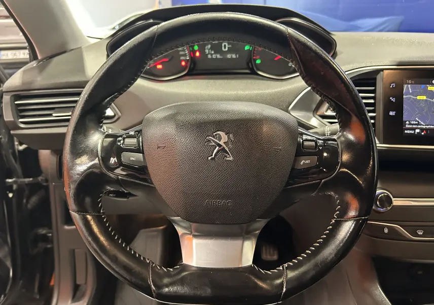 Vue rapprochée du volant en cuir noir du Peugeot 308 SW 2018, avec tableau de bord et écran GPS visibles.