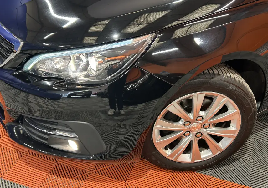 Gros plan sur l'avant droit noir brillant du Peugeot 308 SW, mettant en valeur le phare et la jante alliage.