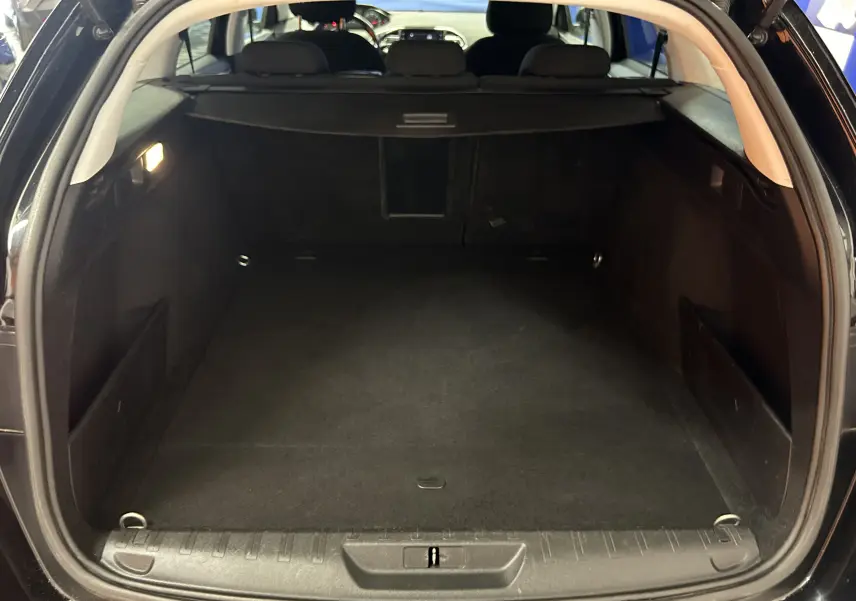 Coffre ouvert d'une Peugeot 308 SW noire, vue arrière montrant un espace de chargement propre et spacieux.