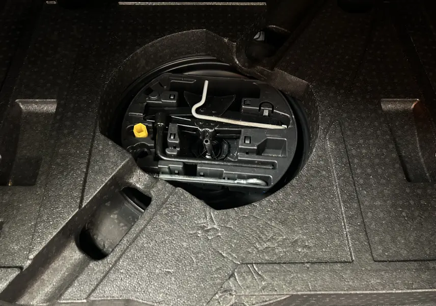 Gros plan sur le compartiment de rangement sous le plancher du coffre du Peugeot 308 SW noir, montrant les outils de bord.