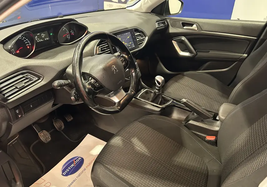 Vue intérieure côté conducteur de la Peugeot 308 SW noire, montrant le volant cuir, tableau de bord et levier de vitesses manuel.