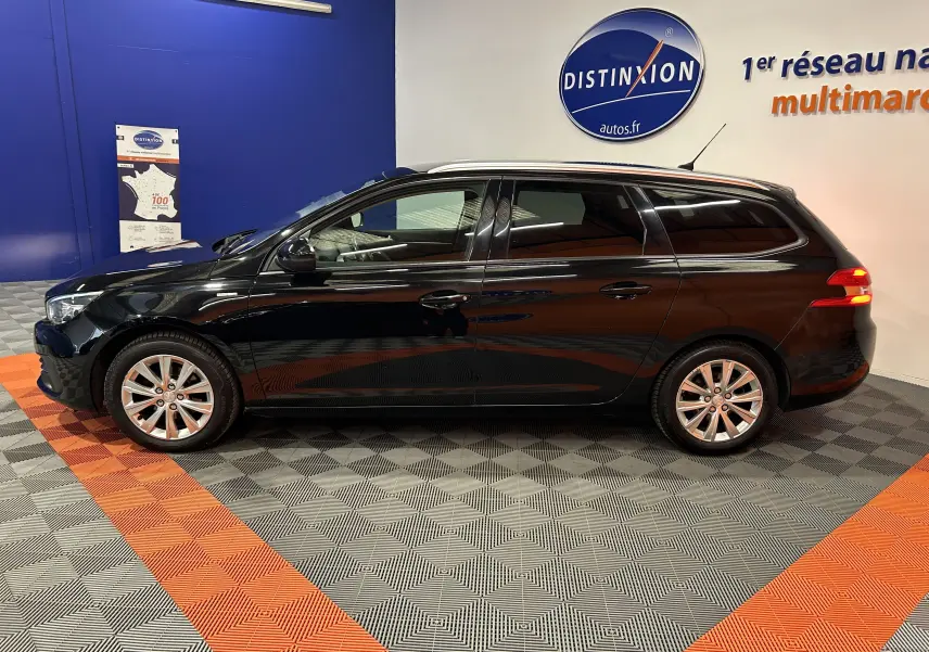 Profil côté gauche d'une Peugeot 308 SW noire de 2018, break diesel avec attelage, en intérieur showroom.