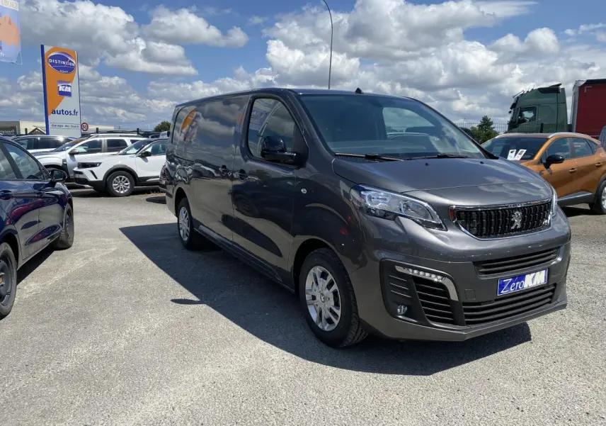 Peugeot Expert Fourgon gris platinium vu en 3/4 avant droit sur un parking sous ciel partiellement nuageux.