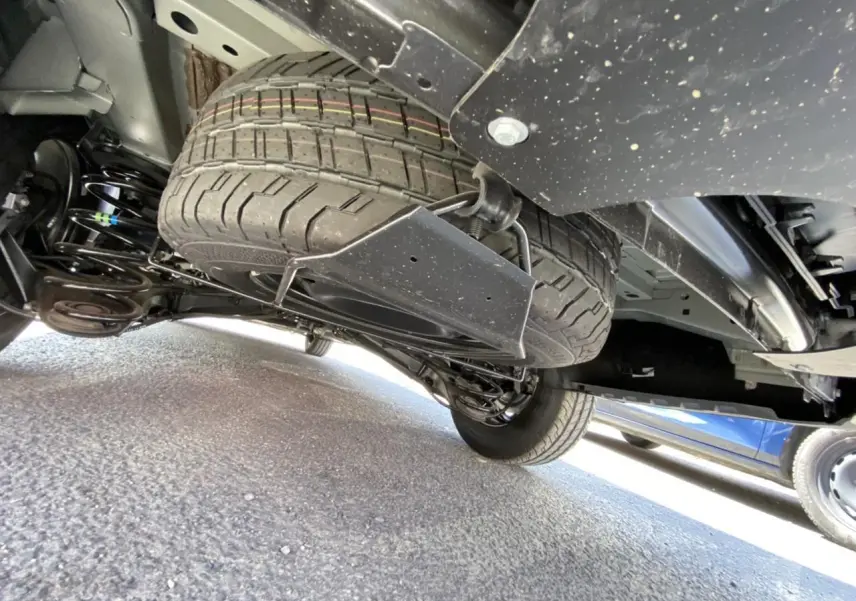 Vue en contre-plongée sous un Peugeot Expert Fourgon gris platinium, montrant la roue de secours suspendue sous le châssis.